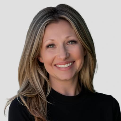 A woman with long, straight, light brown hair and blue eyes smiles at the camera. She is wearing a black top and is posed against a plain, light gray background.