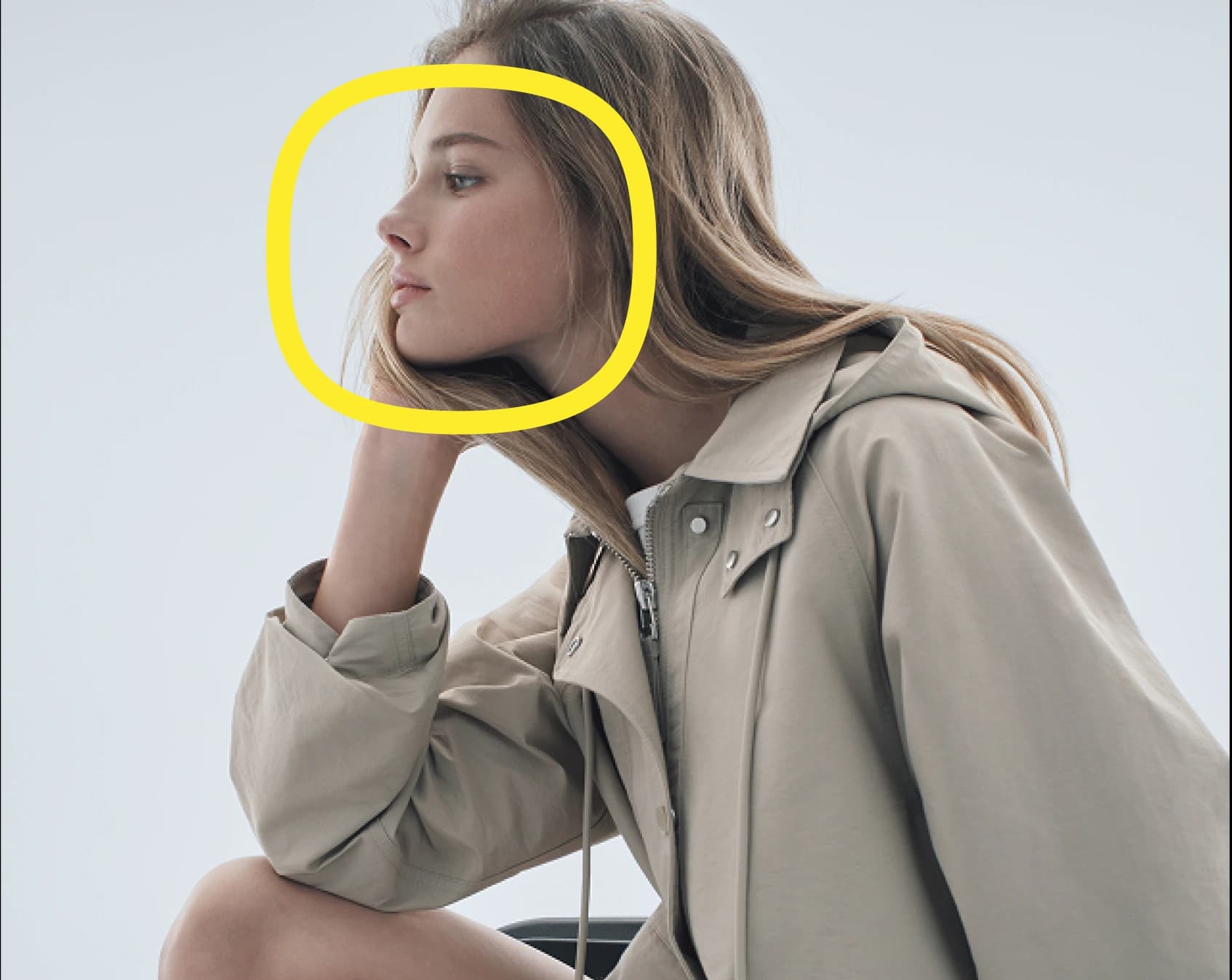 A person in a light beige jacket sits with their chin resting on their hand, gazing thoughtfully to the left; their face is highlighted by a yellow circle.
