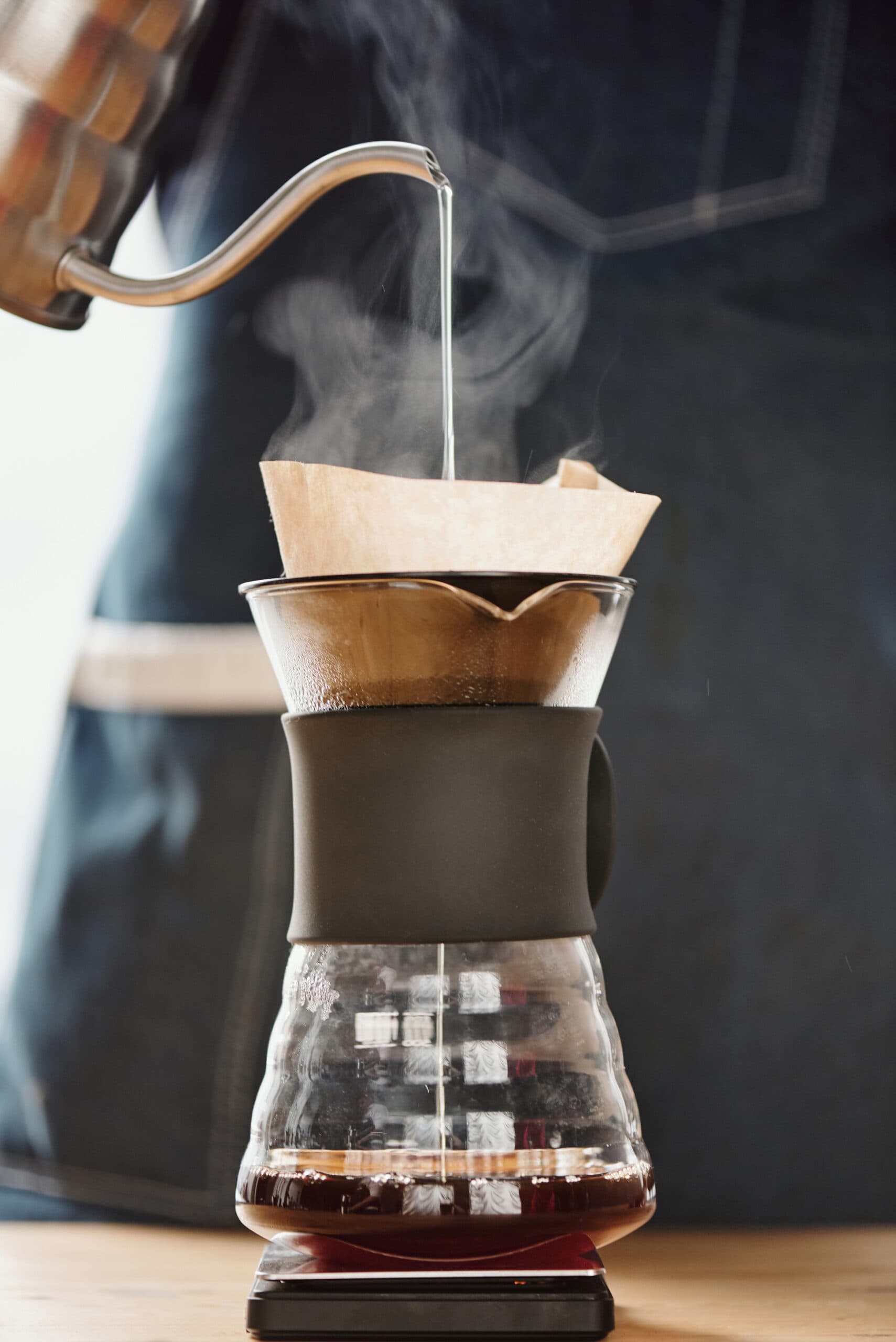 Close-up of hot water being poured from a kettle into a Chemex coffee maker with a paper filter, brewing coffee.