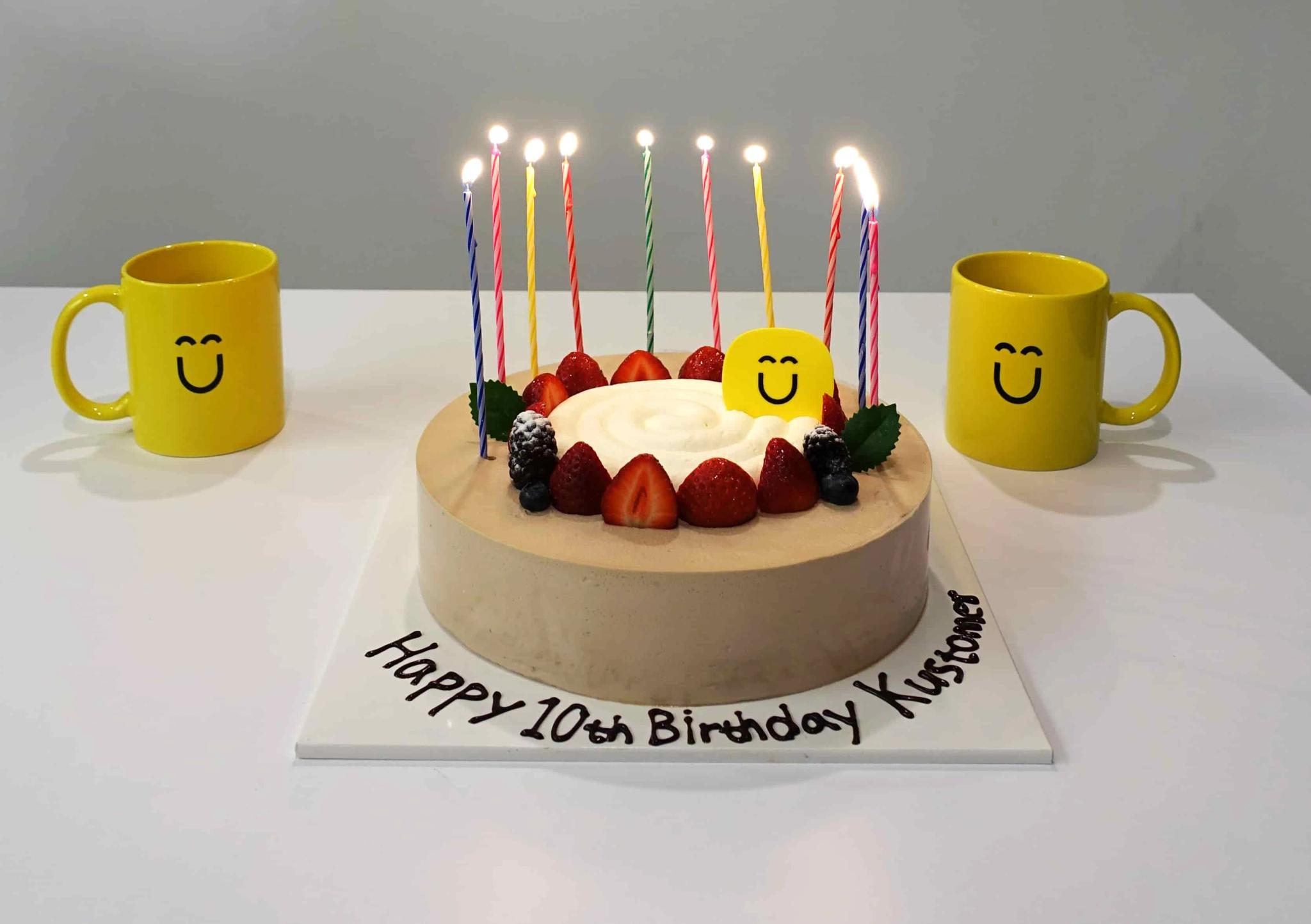 Image of a cake with 10 candles that says Happy 10th birthday Kustomer on a white table