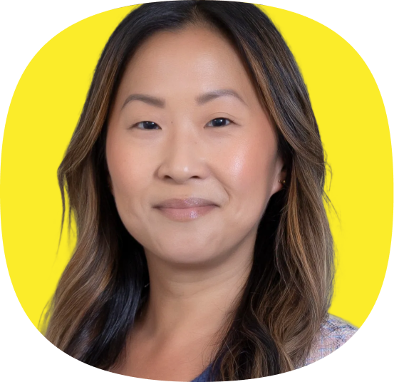 A woman with long, wavy brown hair and light makeup smiles softly in front of a bright yellow background, embodying the warmth and ease of Modern CX from Kustomer Checkout to Retention. She is wearing a light-colored top.