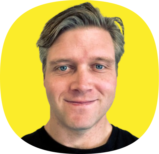 A man with light brown hair and blue eyes smiles at the camera against a bright yellow background, wearing a black shirt—evoking the optimism of modern CX, from Kustomer Checkout to Retention.