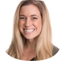 A woman with long blonde hair is smiling at the camera. She is wearing a dark top, and the background is plain white.